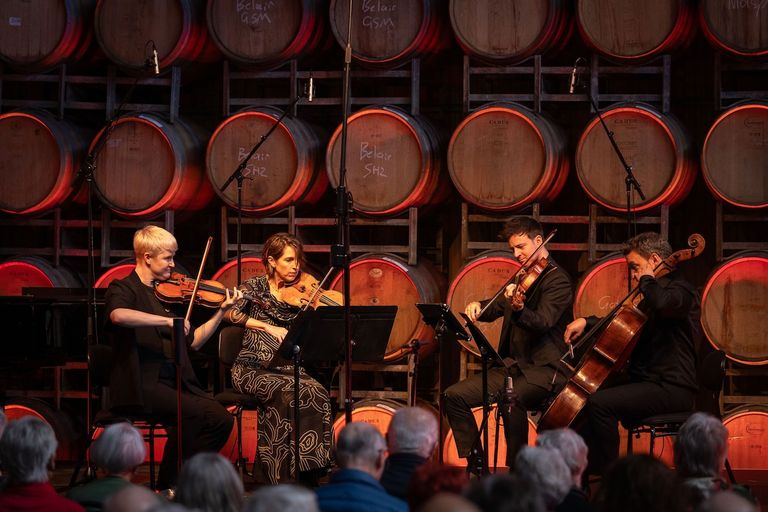 String quartet performs live at Coriole Music Festival 2026 in front of stacked wine barrels inside a winery venue with audience in foreground.